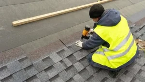 A man in a yellow vest is working on a roof.