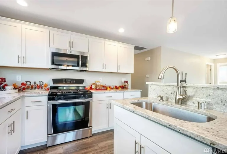 A kitchen with white cabinets , stainless steel appliances , granite counter tops and a sink.