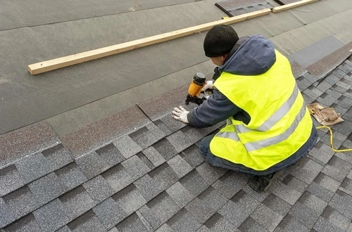 A man in a yellow vest is working on a roof.