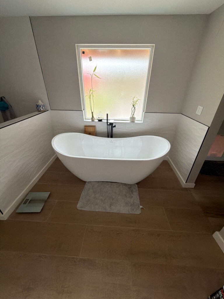 White freestanding bathtub with a black floor-mounted faucet and pale tile on the surrounding walls.
