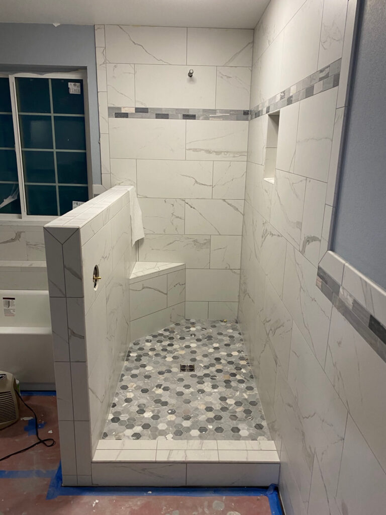Tiled shower under construction with a built-in bench, wall niche, and hexagonal mosaic floor.