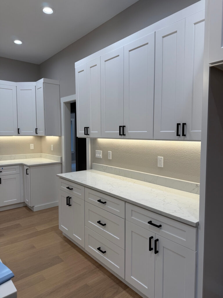 White kitchen cabinets with black hardware, pale countertops, and under-cabinet lighting.